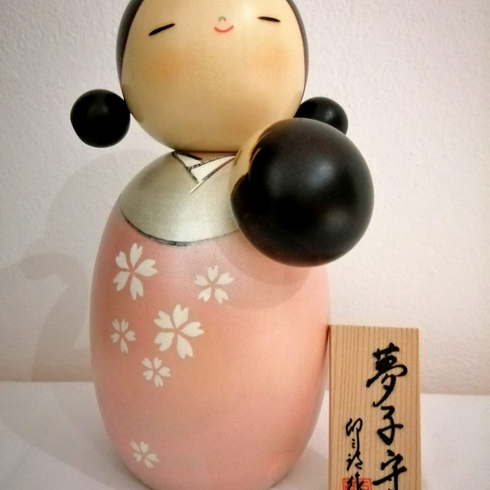 Kokeshi maternità, nome originale Yumekomori. Rappresenta una madre che culla il proprio bambino per farlo dormire in modo sereno e felice, dipinta a mano su legno.