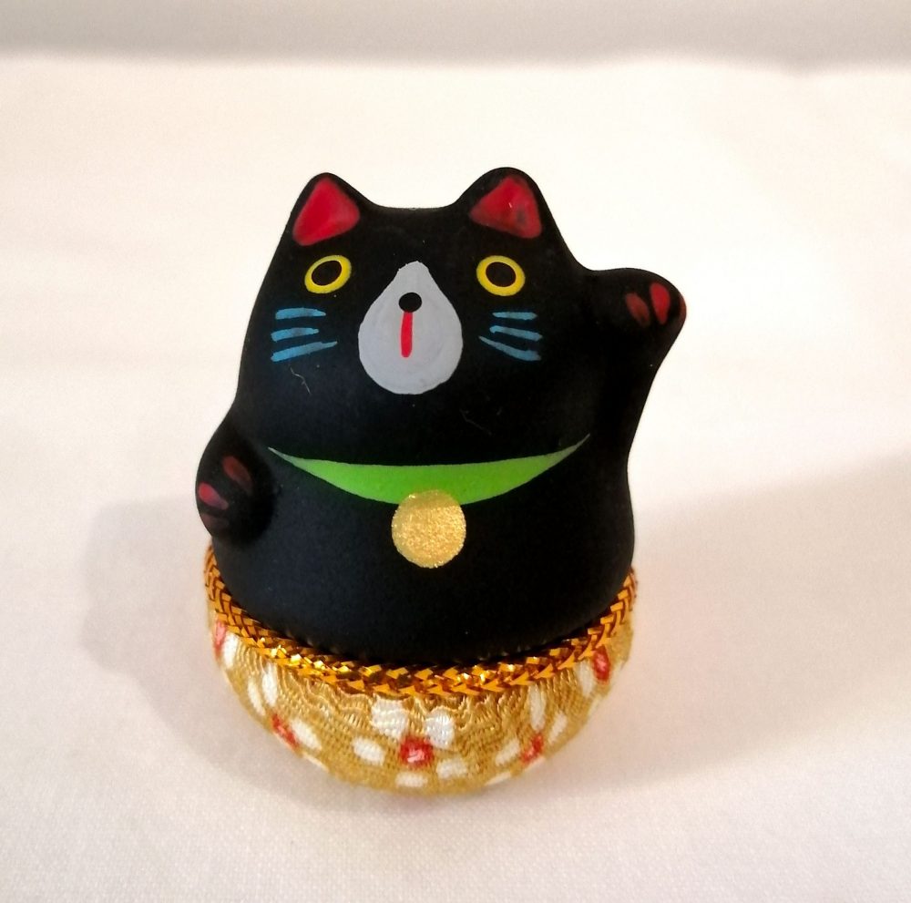 Maneki neko, gatto porta fortuna, di colore nero con base tonda che torna sempre in piedi.