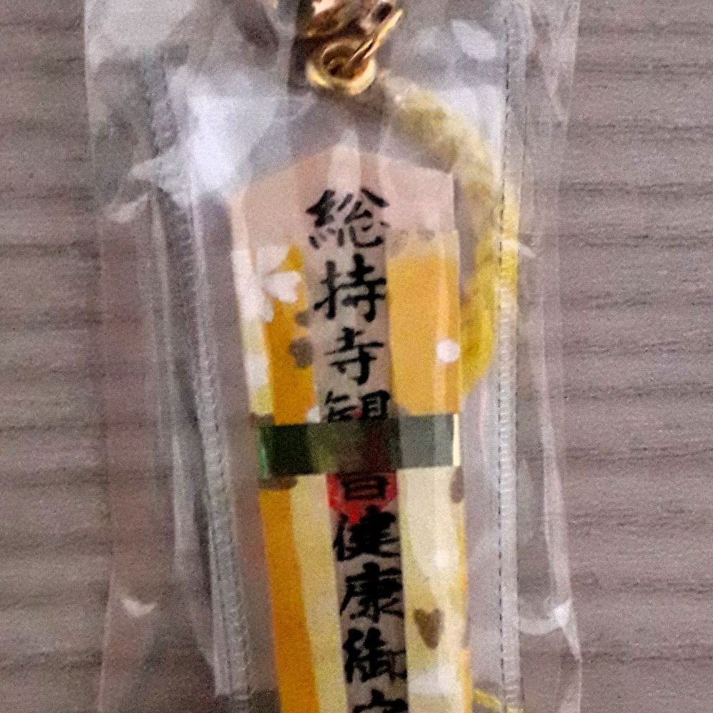 Omamori a ciondolo in legno, rivestito con stoffa di colore giallo, per augurare o augurarsi una buona salute.