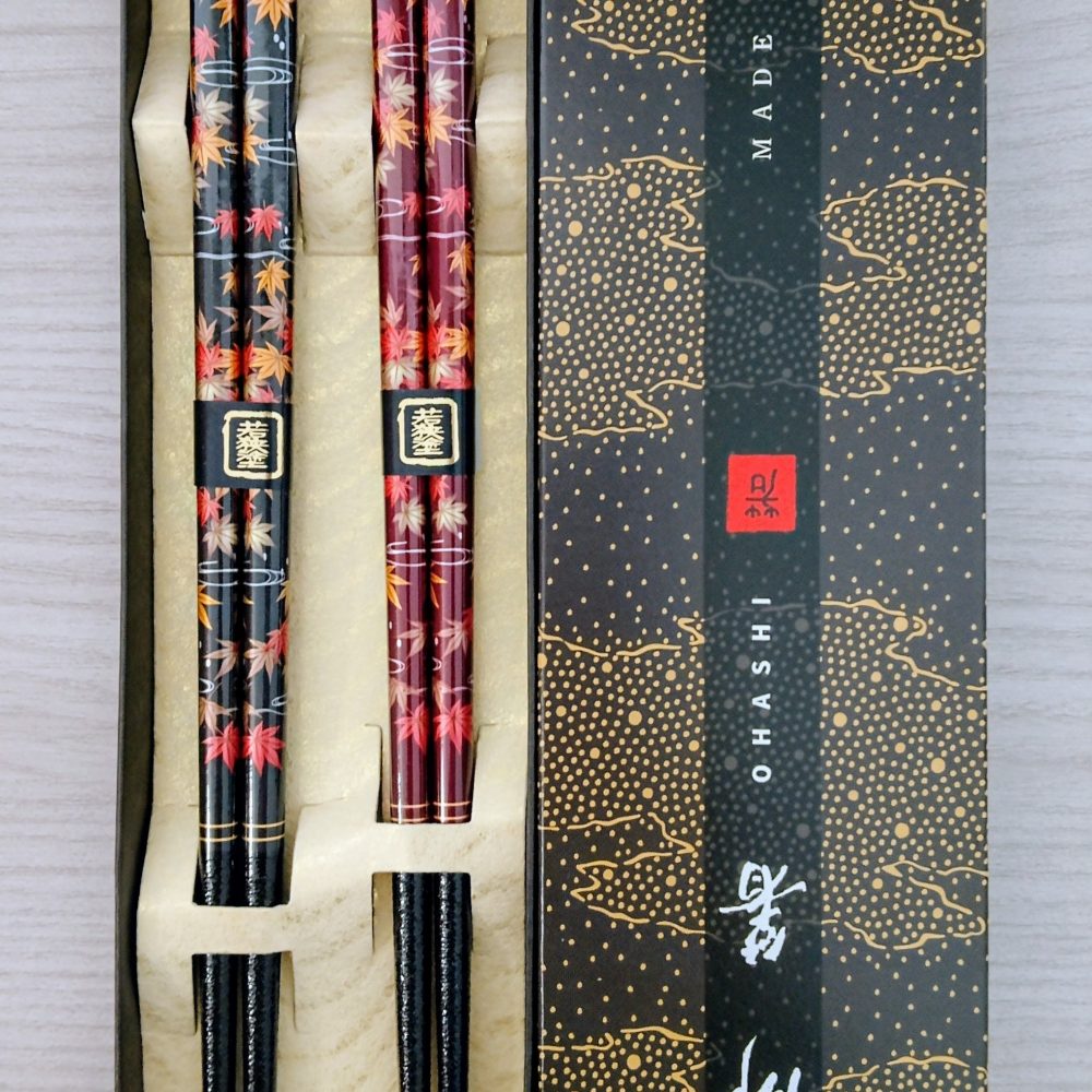 Seghettate in punta per una migliore presa del cibo. Adatte a chi è esperto e a chi si approccia a mangiare con le tipiche hashi giapponesi. Disegno di momiji, foglie di acero con i colori autunnali, una nera e una marrone, eleganti all'interno di una scatola raffinata.