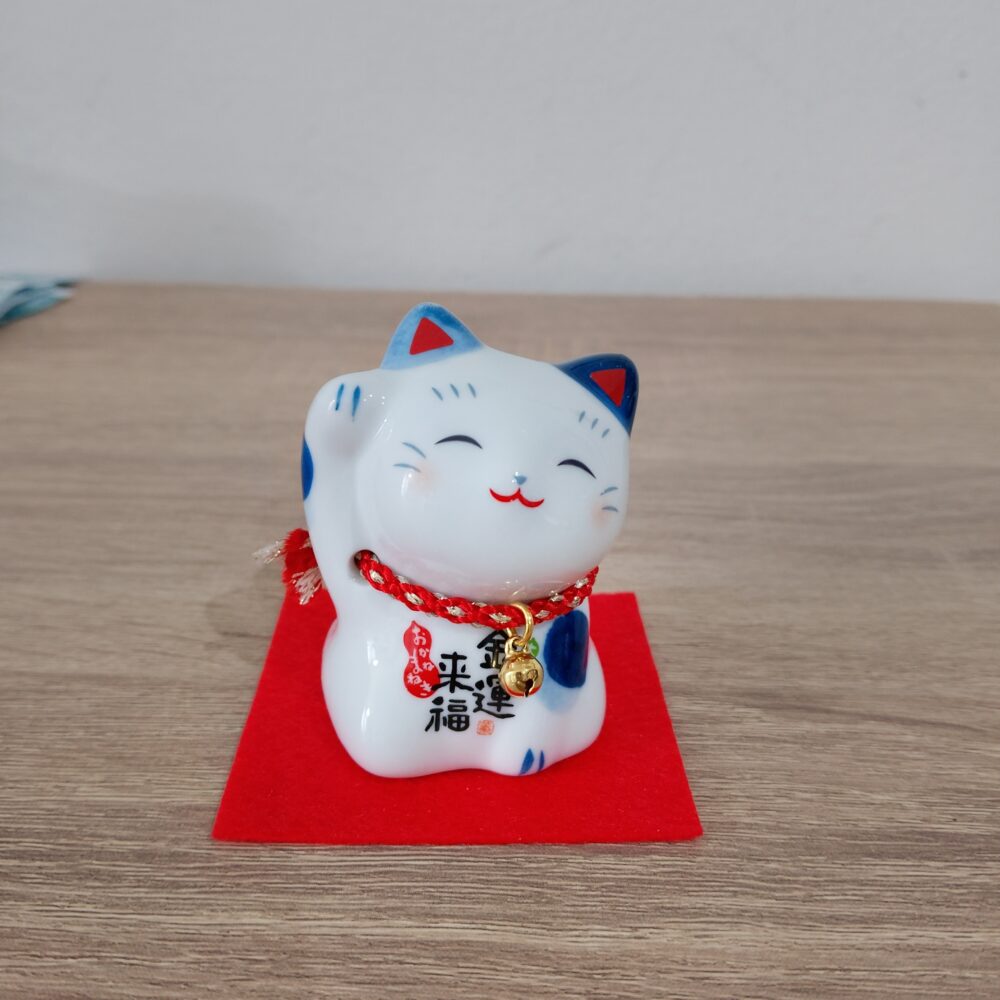 Gatto giapponese, Maneki Neko, letteralmente "gatto che chiama" ,tipico  porta fortuna, spesso utilizzato anche nelle attività commerciali per attirare clienti, fortuna e denaro, in base alla zampa che tiene alzata. Dolce gattino bianco con macchie azzurre, dipinto a mano, tiene la zampa destra alzata, il ché significa che attira soldi e ricchezza.